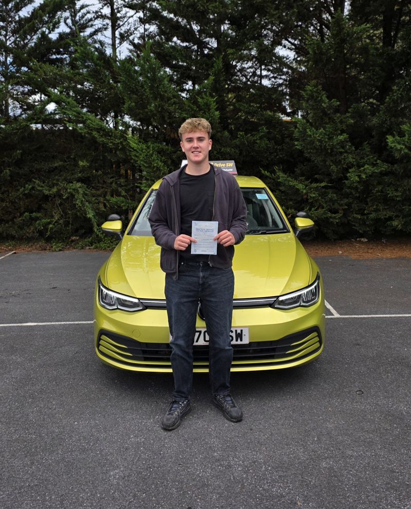 Charlie holding his driving test pass certificate in front of the driving school car