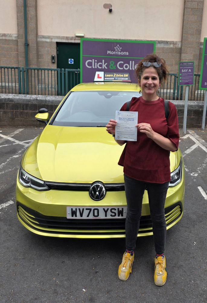 Danielle holding her driving test pass certificate in front of the driving school car