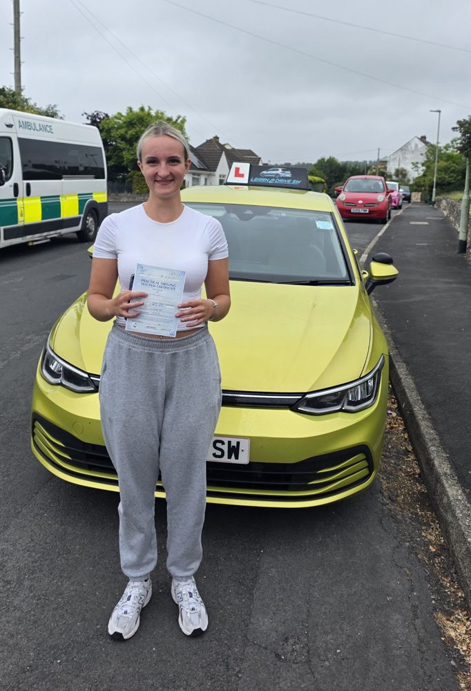 Ellie holding her driving test pass certificate in front of the driving school car