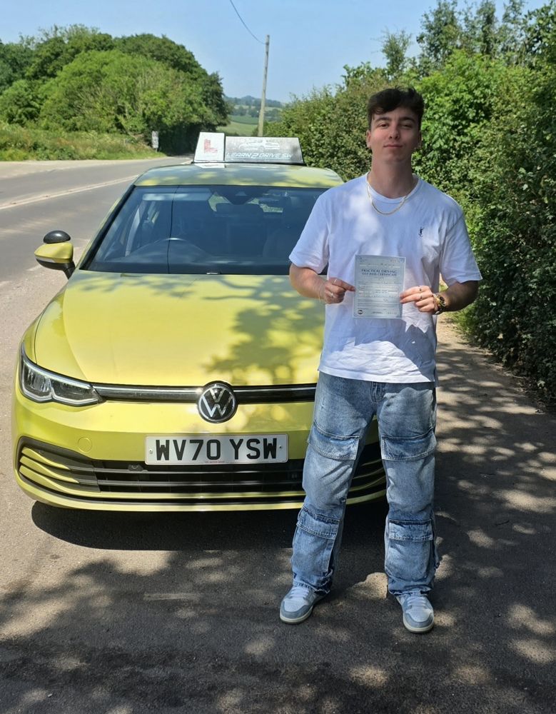 Oliver holding his driving test pass certificate beside the driving school car